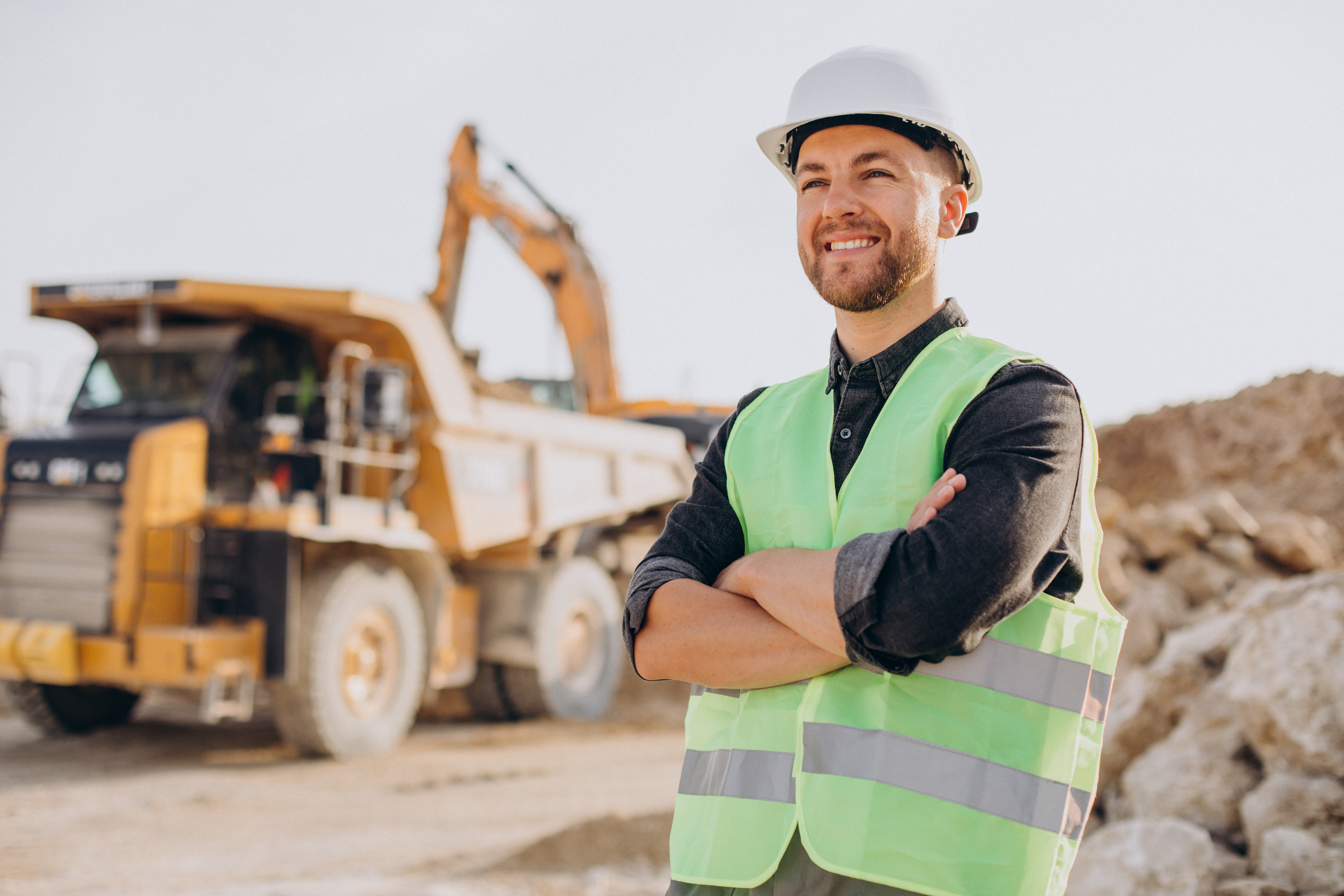 A worker in a hi-vis vest and hard hat at a quarry with heavy machinery